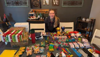 Photo of a white teenage girl sitting behind a table full of Christmas items.