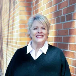 Photo of a smiling white woman posing in front of a brick wall
