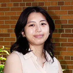 A photo of an Asian woman smiling posing in front of a brick wall.