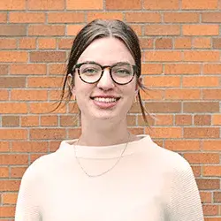 Photo of a smiling white woman with glasses posing in front of a brick wall